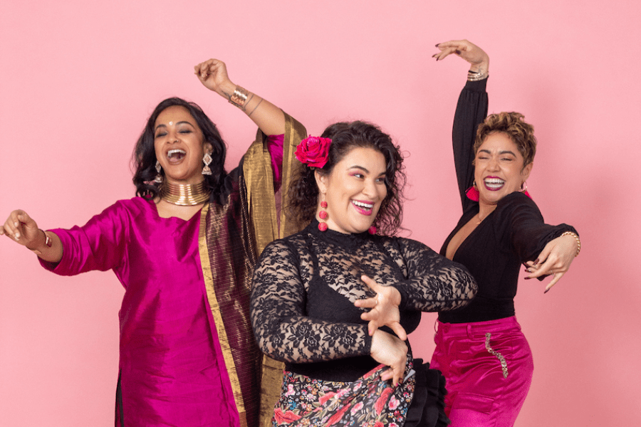 Three performers strike poses in front of a pink background.