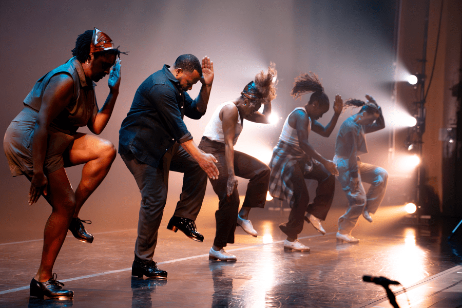 Four performers on a row strike poses mid dance on a stage.