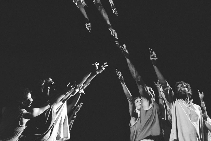 A black and white image, dancers hold their hands up to the ceiling and hands are held down to them - in either a projection or through photoshop.
