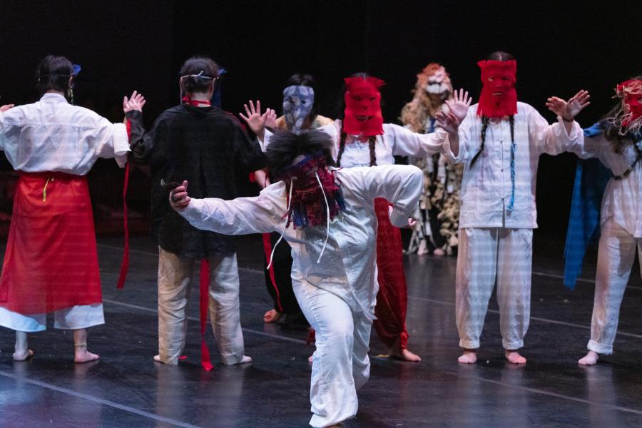A group of masked performers on stage dance.
