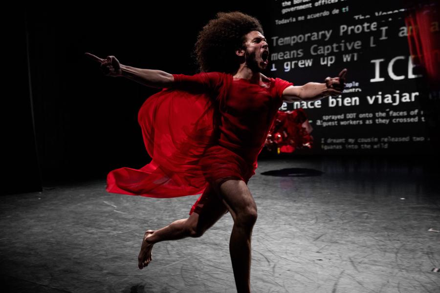Miguel runs in a red dress. They scream and there's text on on the backdrop behind them.