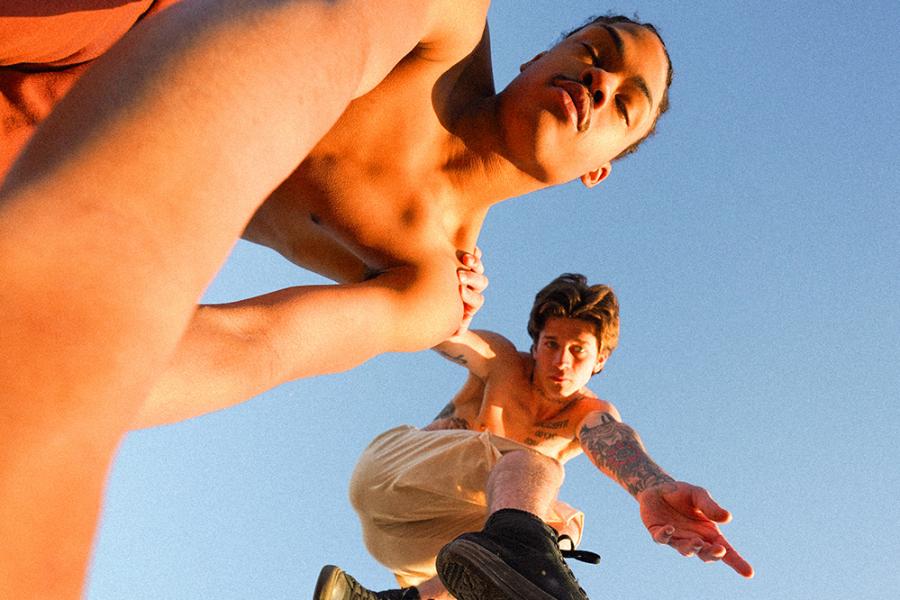 One dancer leans, for a selfie, on another while leaping through the expansive blue sky.