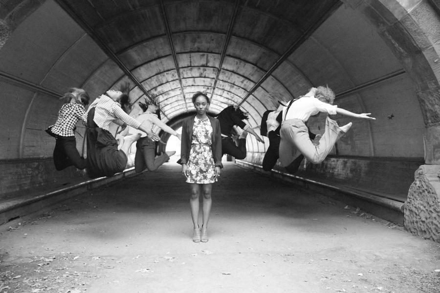 In a tunnel, one dancer stands still in the middle while others leap to her left and right.