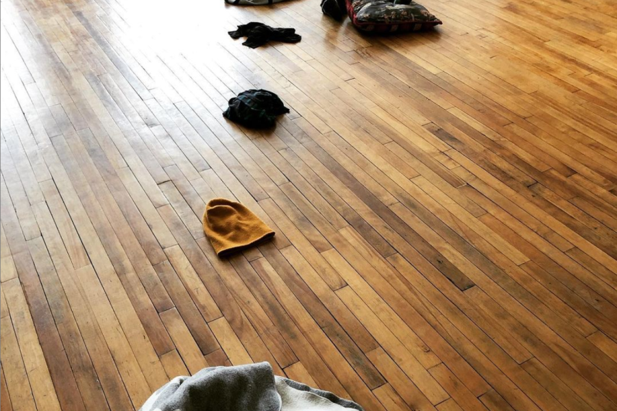 A dancer lays on a wooden floor next to clothes she just took off.
