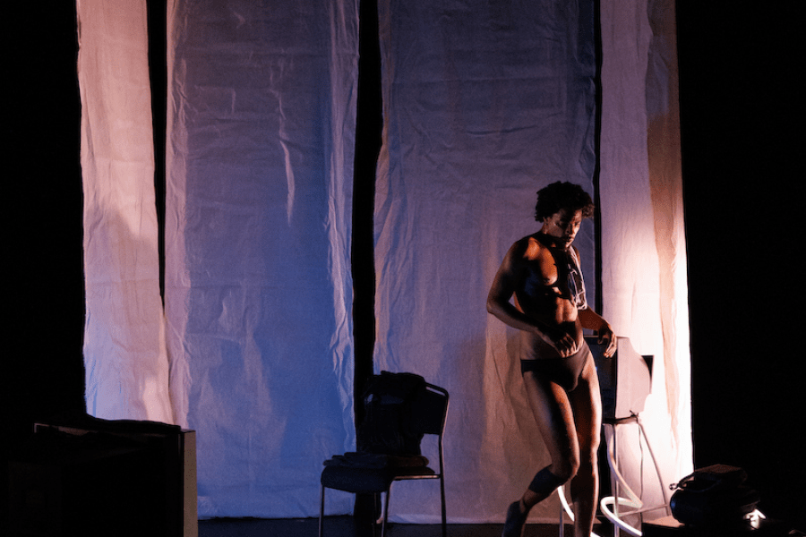 A lightly dressed performer stands in front of a white curtain.