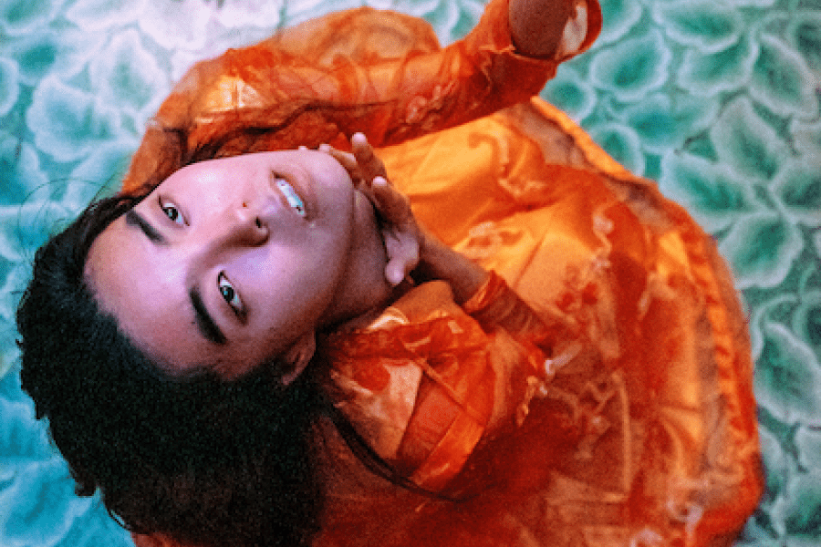 From above, a person dressed in orange is shown looking upwards while standing on a floral patterned blue floor.