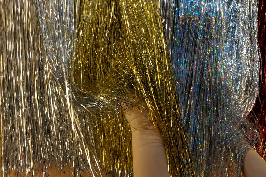 Hands rustle through gold and silver tinsel hanging on wall.