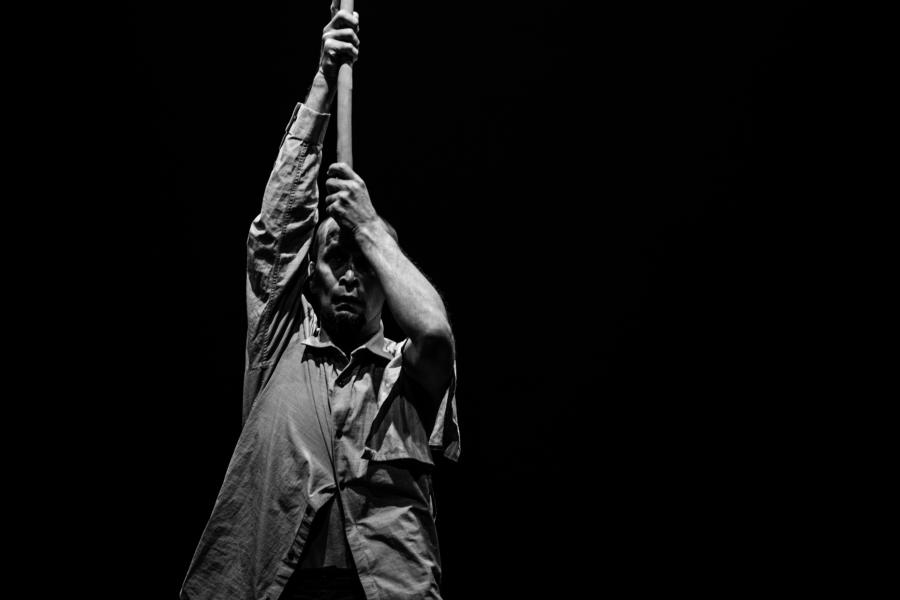 Black and white: an Asian man holds a wooden pole over his head.