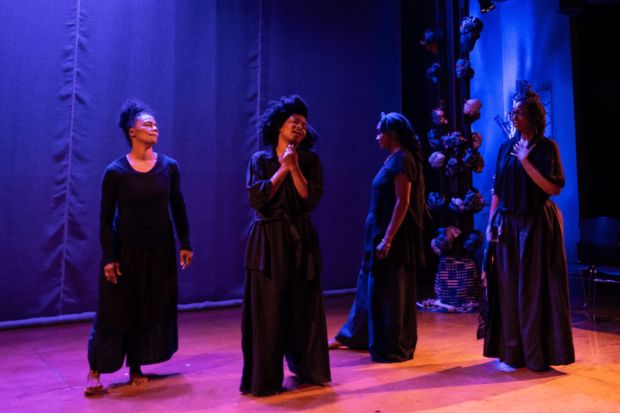 Four people dressed in black stand on a stage.