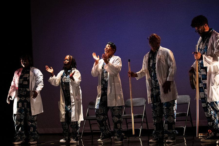 The band from the previous photos stands. They are the folks wearing lab coats. They clap and stomp poles.