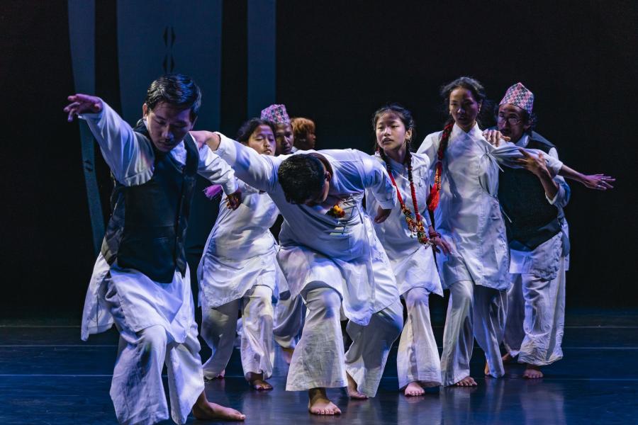 A group of performers dressed in white dance together on a stage.