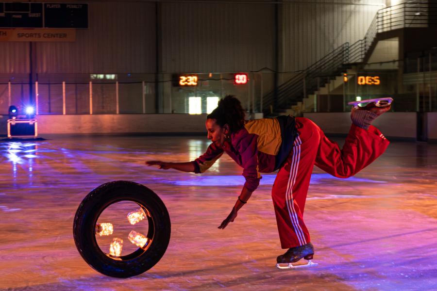An ice skating performer chases a tire full of lights in a skating rink.