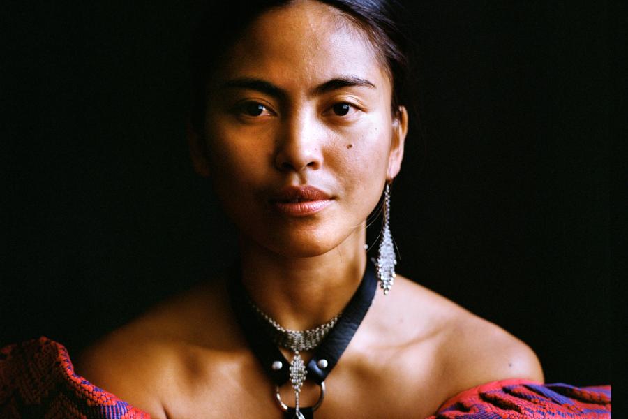 A headshot of a person with dark hair and dangling silver earings.