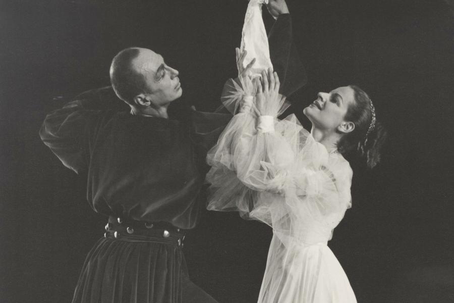 A black and white photo of two people, one dressed fully in black and the other dressed fully in white dance together.