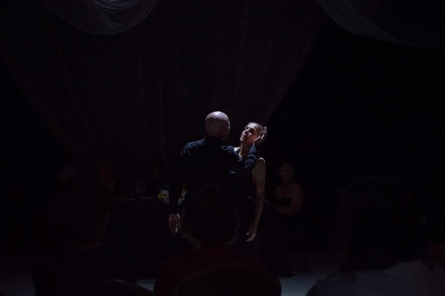 A stark overhead light catches the tops of two individuals in a dramatically dark image.