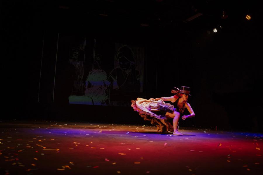 A performer in a frilled dress poses on a stage.