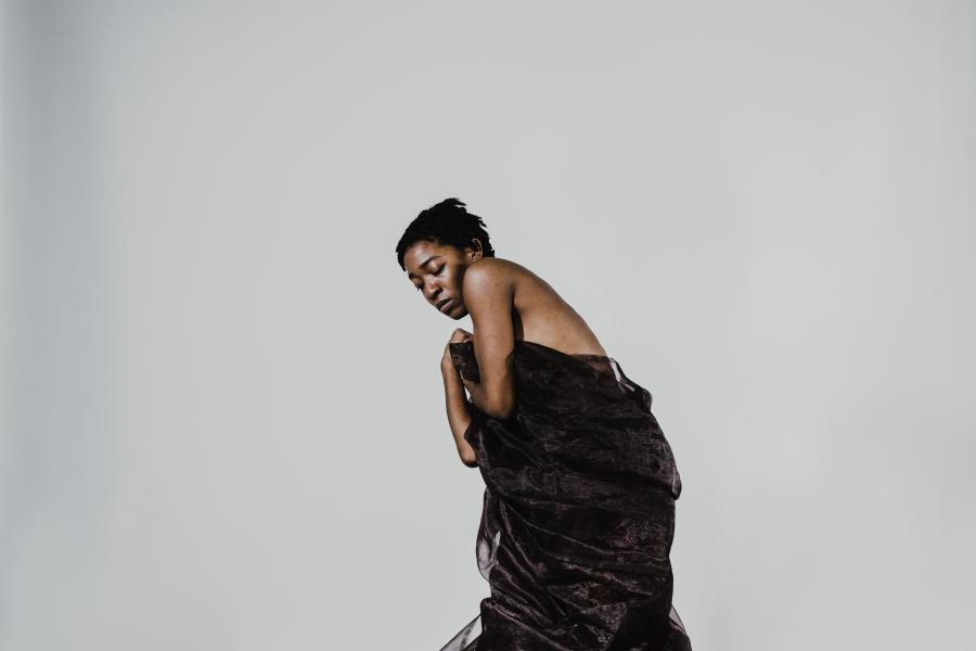 A person stands in front of a white background wrapped in a dark cloth.
