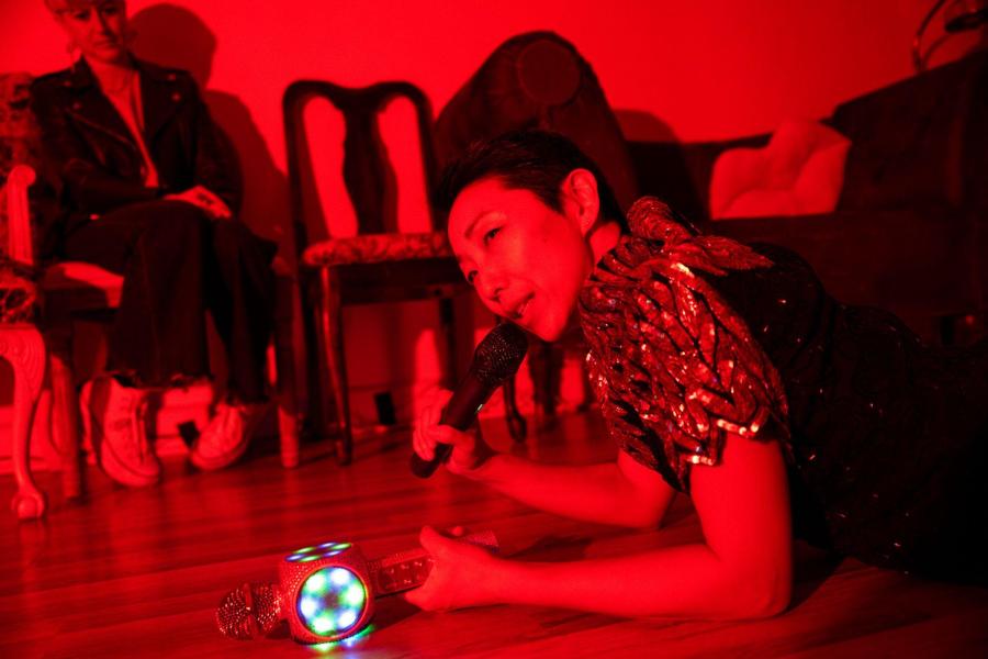 In a room flooded with red light a person lays on the ground while holding a microphone.