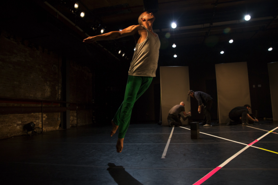 A dancer leaps over a floor with tape in diagonal lines along it.