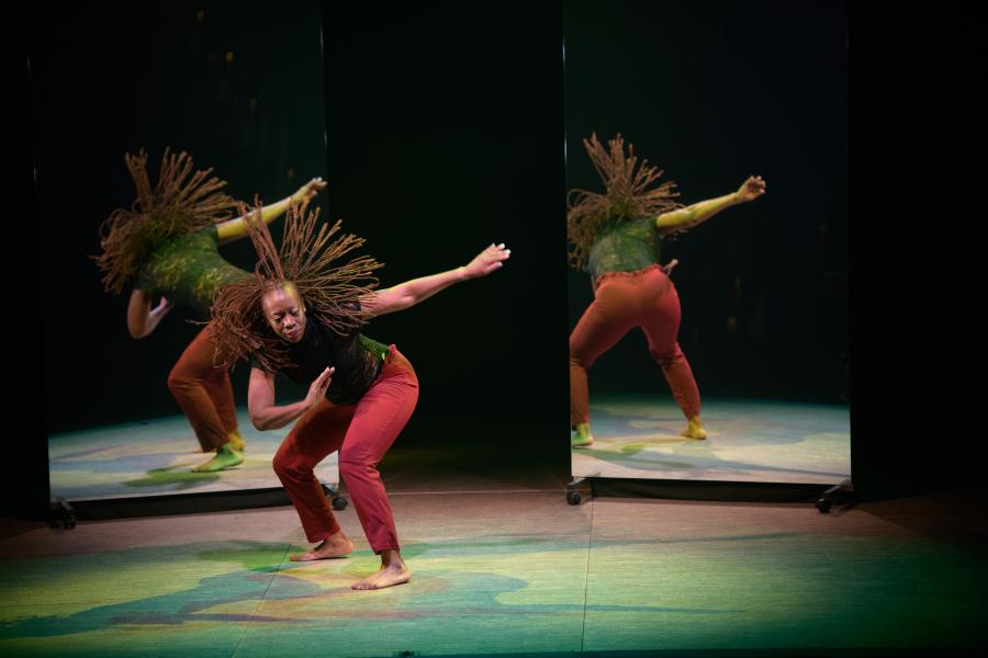 Hair still swinging from a dance move, a performer strikes a pose in front of two mirrors which reflect them.