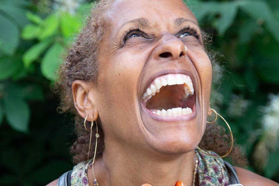 A Black woman smiles and holds her chest, while looking to the sky.