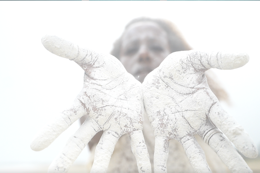 Closeup and blown out: a Black woman holds her sand-covered hands out.