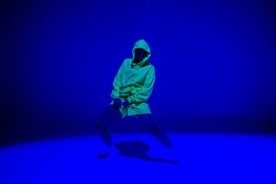 Person in a neon yellow hoodie dances in a space lit by blue light