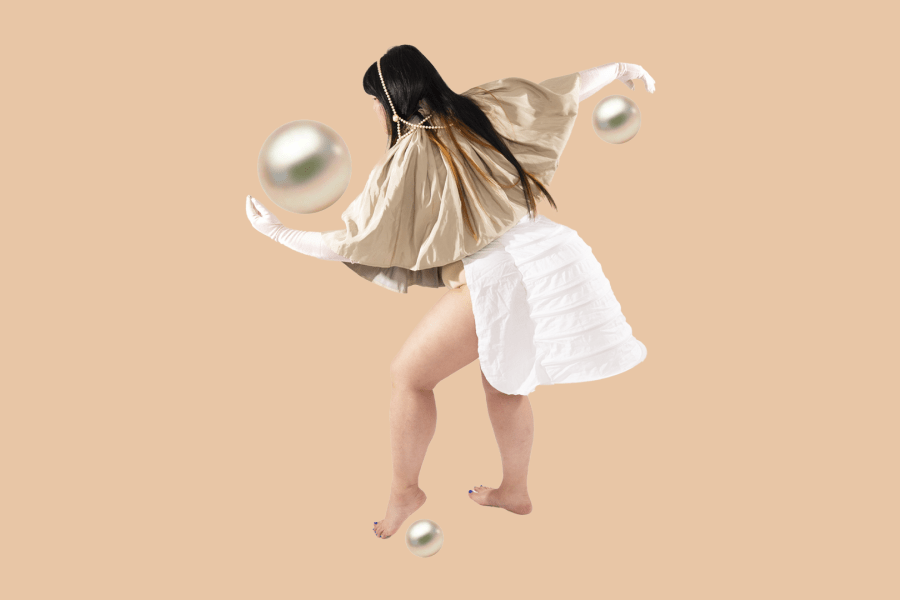 In front of a tan colored background a long haired person wearing a golden top stretches out their arms to the front and back. Three pearls of great size are shown by their hands and left foot.