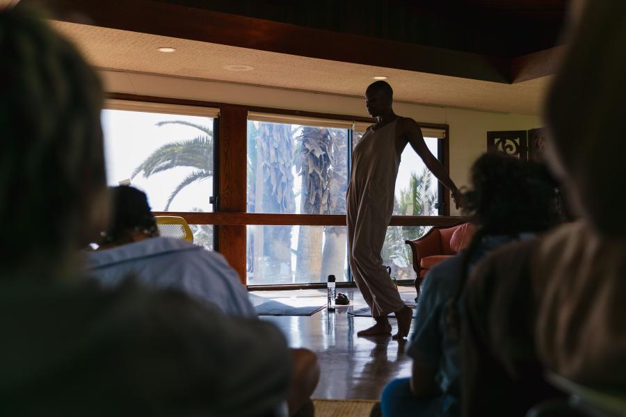Seated observers watch a performer lean their arms back.