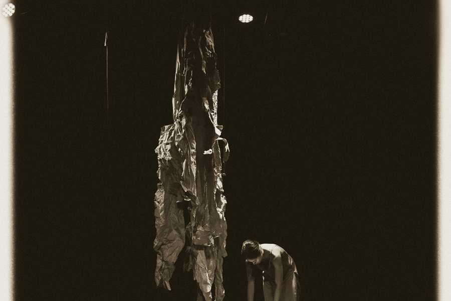 A black and white photo of a person reaching into a metal basin in the middle of a dark stage.