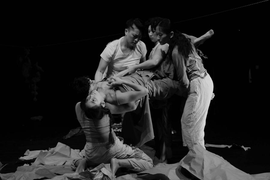 A black and white photo of four performers holding a person in the air.