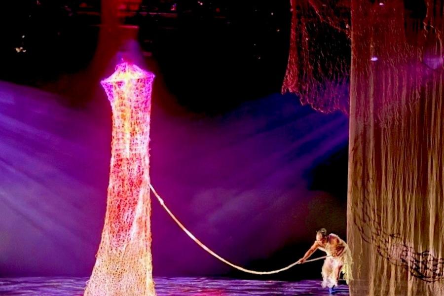 A performer on a stage holds a rope connected to a net which hangs from the ceiling.