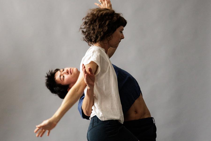 Two performers are intertwined in front of a gray background. 