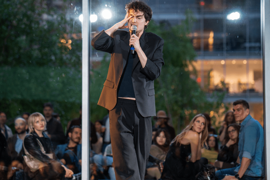A barefoot performer dressed in black stands on a stage while holding a microphone.