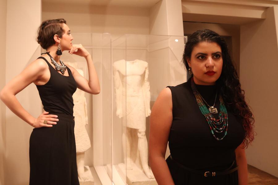 In a gallery, two women pose next to headless statues.