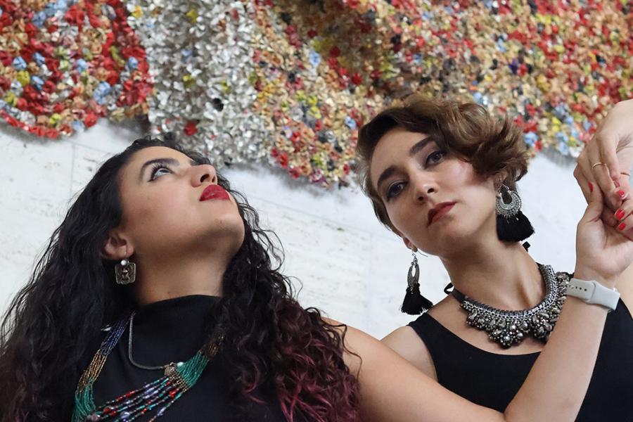 In front of a beaded curtain, two women dance and pose.