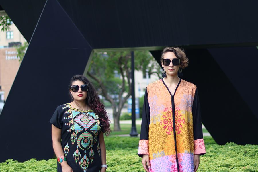 On a museum lawn, two women pose blankly. They were colorful robe-like gowns.