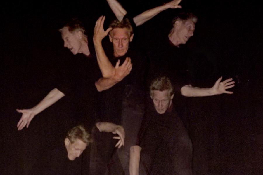 A performer dressed in black strikes a pose in front of a background covered in projections of them striking poses.