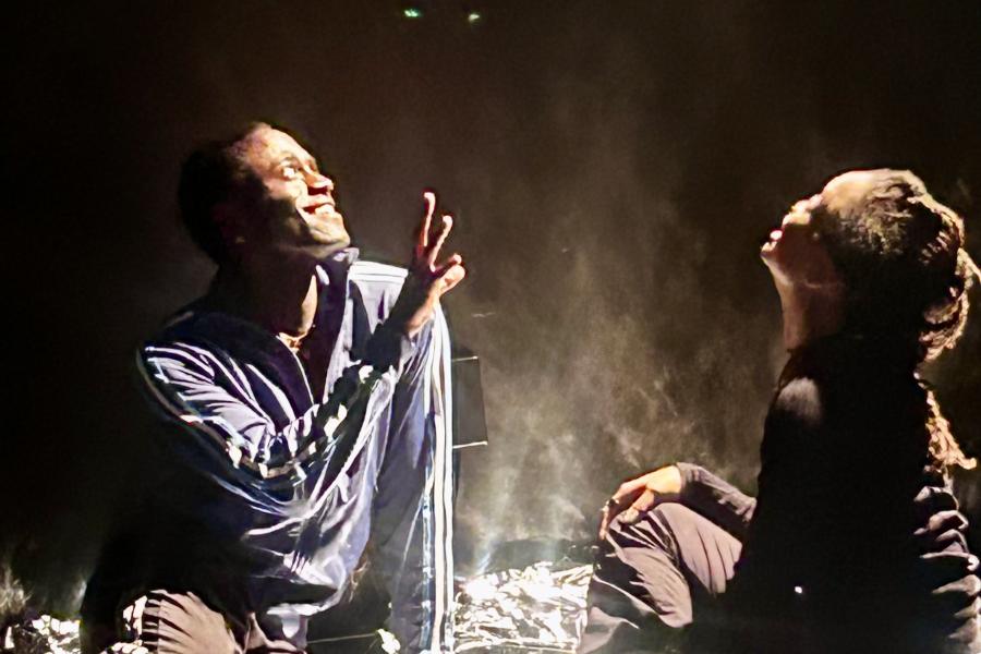 Two people sit on a square of tinfoil on a stage.