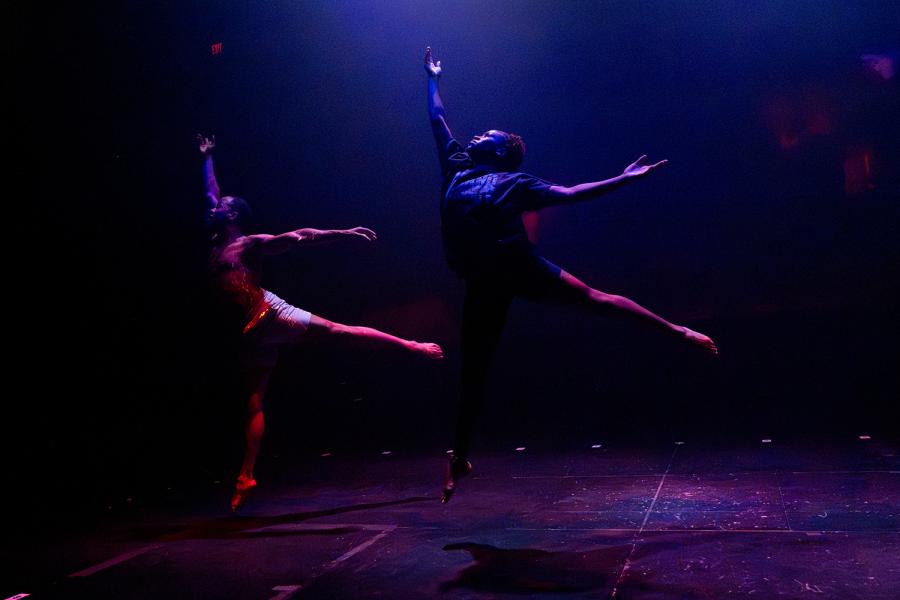 Two dancers leap onto one foot with their arms up and their left legs back.