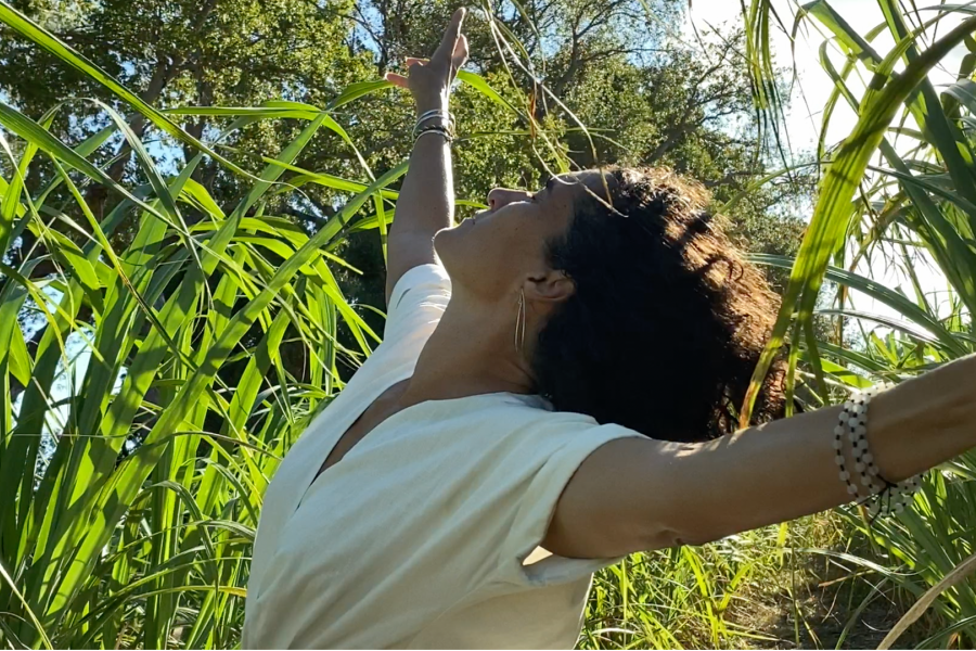 In tall reeds, a woman grazes the grass and looks to the sky.