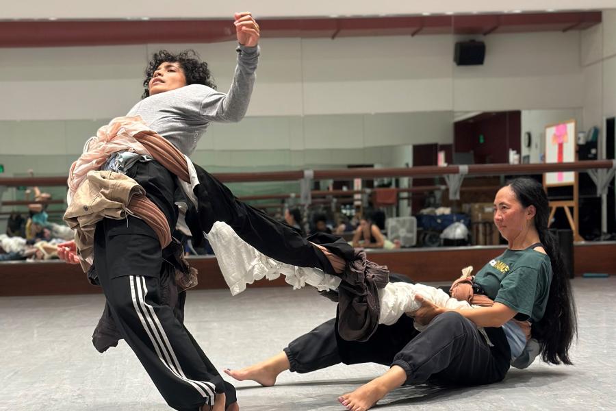 A woman, on the ground, tugs on fabric wrapped around the body of another woman who leans back towards her.
