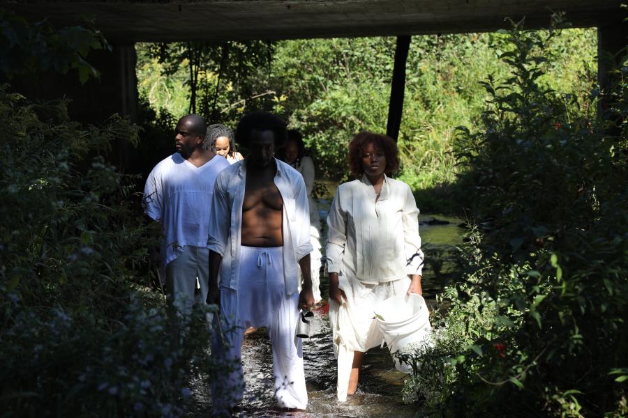 Five Black folks walk through the woods while wearing all white.