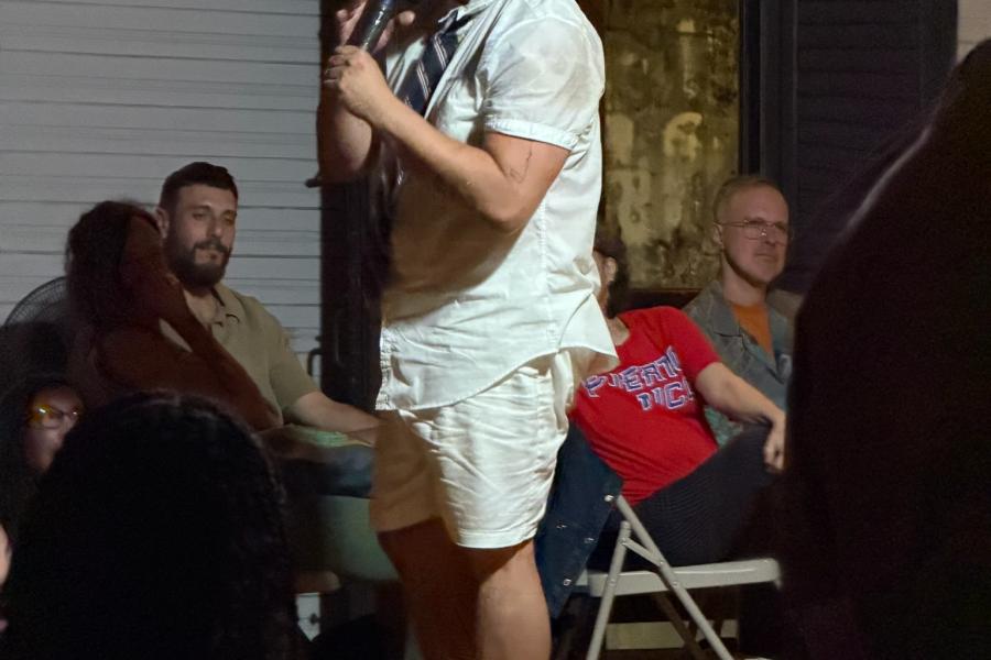 In a room full of seated spectators, a person whose face has been painted white stands holding a microphone.