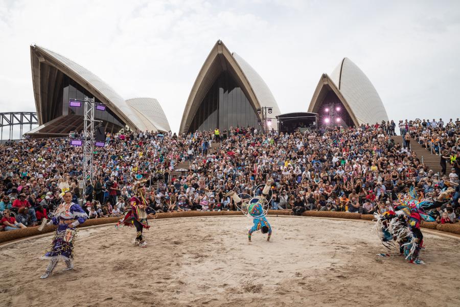 Outside the Sydney Opera House, a crowd watches four dancers do flips.