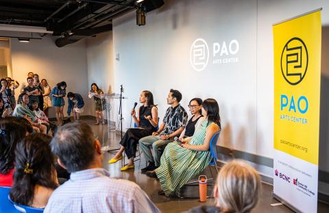 Four east Asian folks sit. An audience watches. Signs say "PAO Arts Center."