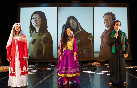 In front of screens with projections of each of the actor's headshots, three performers stand. Two women and a man, who holds a microphone.