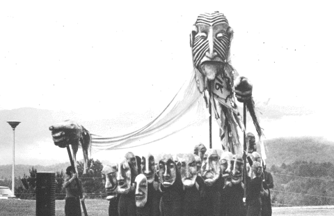 Orange NEFA 50th Logo over purple. A black and white image of a large puppet head with a band of folks in matching masks in the mountains. 