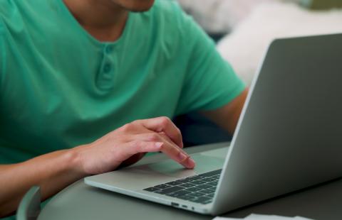 A brown man types on his laptop.