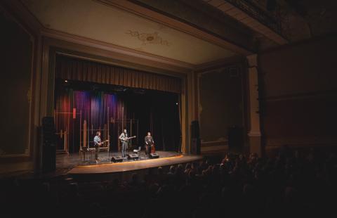 A trio performs on a stage. The glow from the stage lights the rest of the theater.